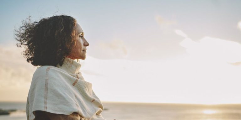 Mature Woman Wearing A Pashmina Leaning On A Railing And Looking Out At The Sunset Over The Ocean.jpg