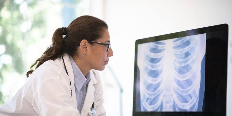 Doctor Of Latino Ethnicity Leans On Her Desk And Looks At A Radiogram Of A Chest On Her Desktop Computer.jpg